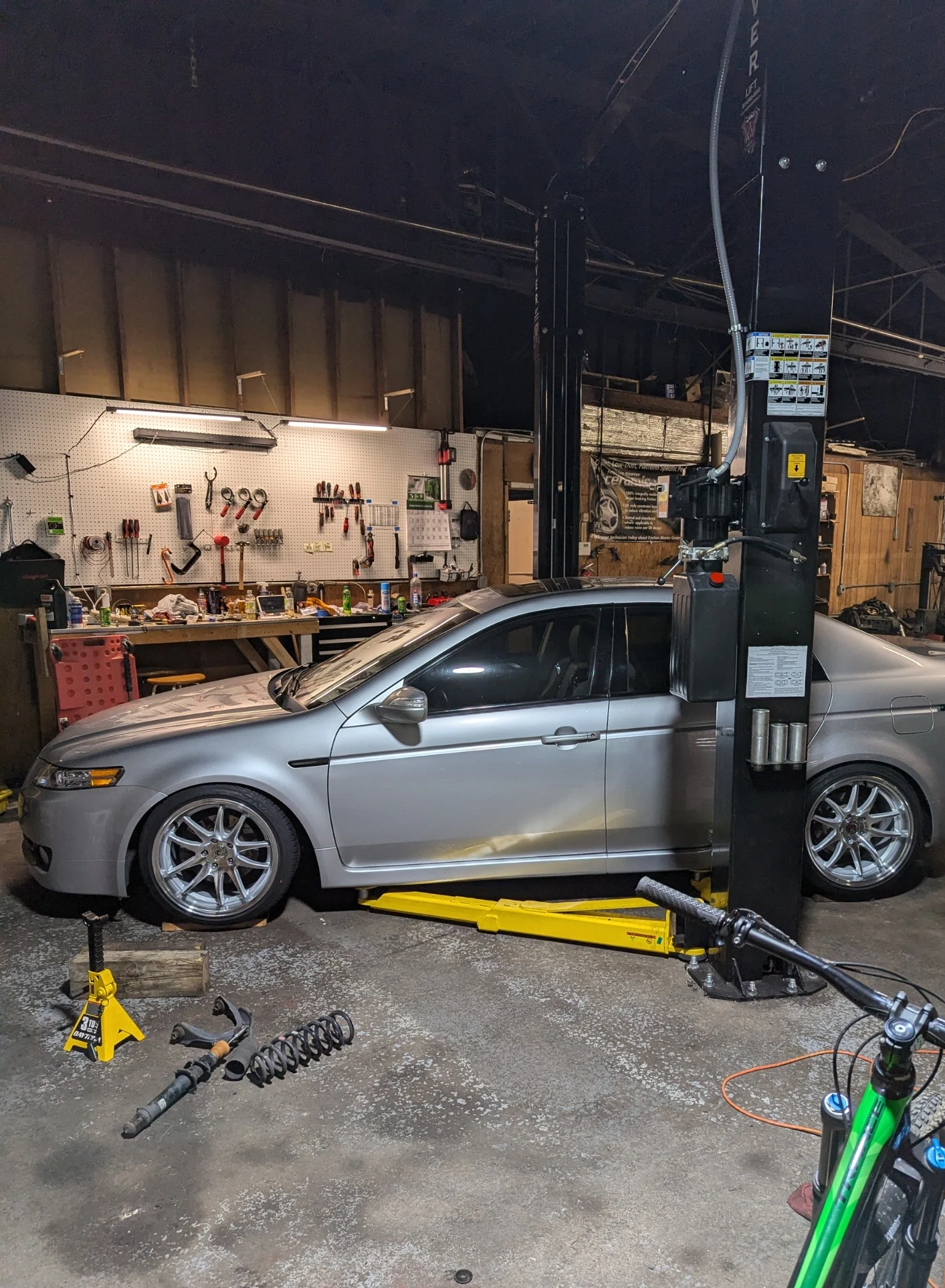 Silver Acura TL on a lift during suspension work at The Engine Block