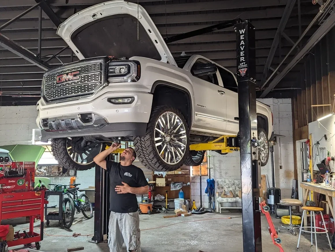 Technician inspecting a lifted GMC truck in a service bay at The Engine Block